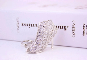 Detailed macro view of silver hollow mesh high heel shoe keychain on white surface