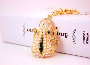 Detail of golden frog keychain with white pearls and green gemstones on vintage book