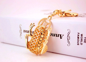 Macro shot of a hollow gold frog keychain with coin pattern and white pearl accents