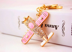 Detail of golden metal biplane keychain with pink enamel wings and sparkling rhinestones