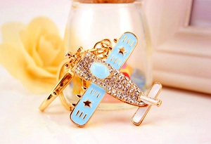 Detailed close-up of a gold metal airplane keychain with crystals and blue wing stars