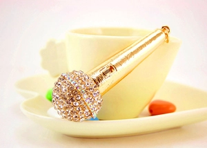 Detailed close-up of a gold microphone keychain with rhinestones inside a ceramic tea cup