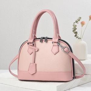 Pink shell tote bag in lychee pattern leather with crossbody strap on a display stand