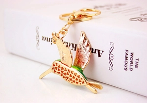 Detailed close-up of a golden metal hummingbird keychain with green neck accent details