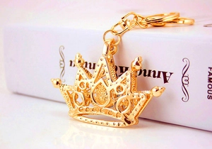 Detailed view of a shiny gold crown keychain with metal clasp on a white book surface