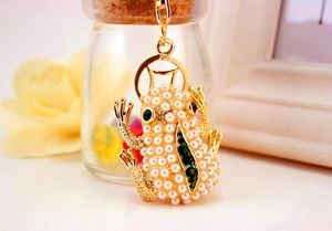 Close-up of golden frog keychain with white pearls and sparkling green gemstones