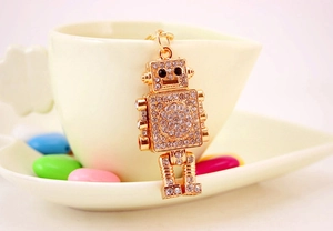 Close-up of golden robot keychain with sparkling rhinestones hanging on a white ceramic cup
