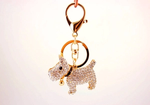 Close-up of golden metal puppy keychain with sparkling crystals and a small gold bell
