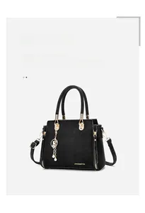Close-up of black crocodile-embossed leather square bag with gold hardware and pearl charm