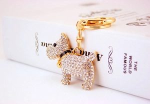 Detailed view of a gold-toned metal puppy keychain with white rhinestones and a small bell