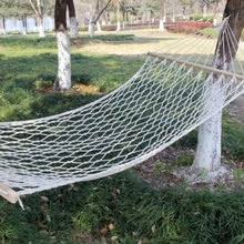 Outdoor white mesh hammock with wooden spreader bars hanging between green trees