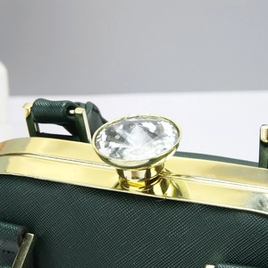 Detalle del bolso de mano verde oscuro con borde dorado y cierre giratorio de cristal