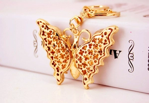 Detail shot of golden metal butterfly keychain with hollow design on a white book surface