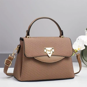 Detailed view of brown woven texture handbag featuring gold shield buckle and leather strap
