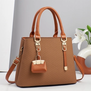 Brown textured women's handbag with top handles and a mini charm in a minimalist setting