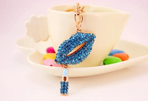 Close-up of a blue rhinestone lip keychain with a lipstick charm on a white ceramic cup