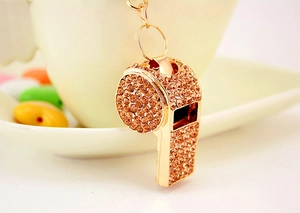 Macro shot of gold whistle keychain featuring dense orange rhinestones on a warm background