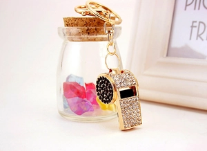 Detailed view of a gold metal whistle keychain embellished with white and black rhinestones