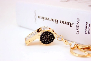 Detailed view of a gold whistle keychain with black and clear rhinestones on a surface