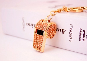 Macro detail of a golden whistle keychain featuring sparkling champagne rhinestones