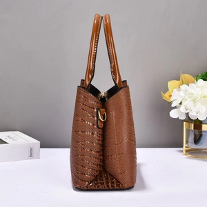 Detail of a brown croc-embossed leather handbag with glossy finish and sleek handles