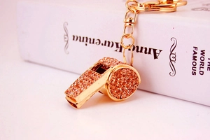 Close-up of golden whistle keychain encrusted with orange pink rhinestones on a book