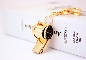 Close-up of golden metal whistle keychain with black rhinestones on a white book