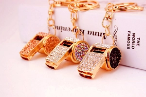 Detailed view of three metal whistle keychains with gold, silver and black rhinestones