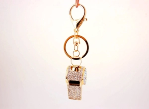 Close-up of golden whistle keychain with sparkling rhinestones on a beige background