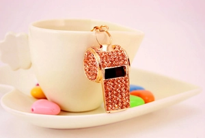 Rose gold rhinestone whistle keychain accessory displayed on a ceramic heart-shaped cup