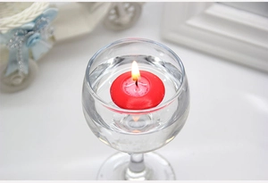 Macro shot of a red round floating tea light candle burning in a clear glass water cup