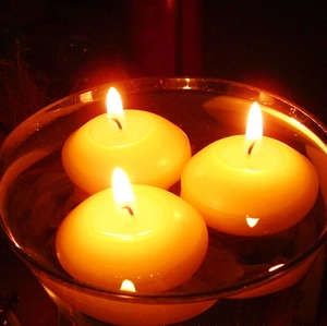 Close-up of three warm yellow floating candles burning in a glass of water for decor