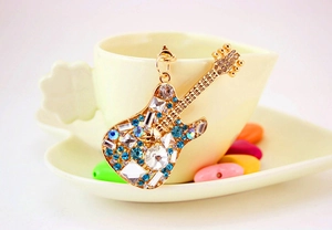 Close-up of golden guitar keychain with colorful rhinestones on a decorative saucer