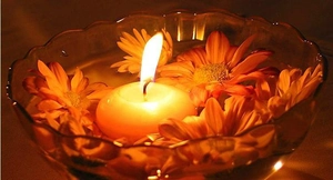 Floating warm yellow tea light candle in a glass bowl with decorative orange flowers