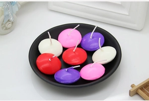 Colorful disk-shaped floating candles in red, pink, purple and white on a black plate