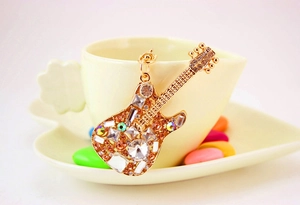 Close-up of golden guitar keychain with sparkling crystals on a yellow teacup edge