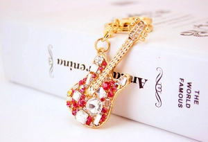 Close-up of guitar keychain with pink and clear crystals on a book surface