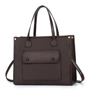 Detail view of brown textured tote bag with woven fabric panel and stylish front pocket
