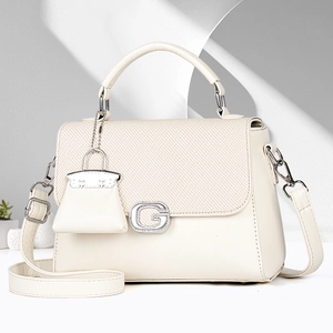 Detalle del bolso de piel crema con solapa trenzada y hebilla en forma de G brillante