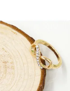 Detailed close-up of golden infinity ring with white crystal inlay on a wooden base