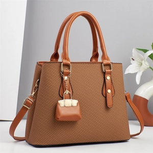 Detail of woven texture handbag with leather handles, golden hardware, and mini charm