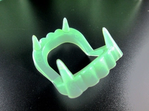 Close-up of green glow-in-the-dark vampire fangs prop for Halloween on a black surface