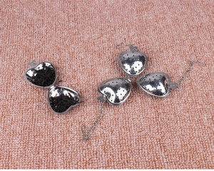 Macro shot of three heart-shaped stainless steel tea infusers with chains on pink fur