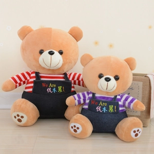 Close-up of two plush teddy bears in striped shirts and denim overalls on wood floor