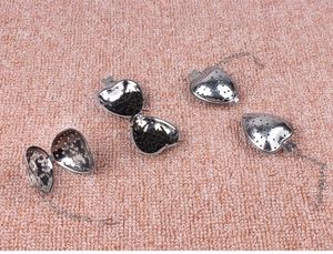 Macro view of heart-shaped stainless steel tea strainers with chains on pink background