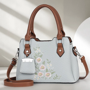 Close-up of canvas handbag with floral daisy embroidery and brown leather handles
