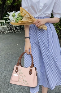 Close-up of elegant floral embroidery and leather handle on a stylish pink handbag
