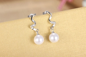 Macro shot of silver pearl drop earrings with spiral diamond accents on warm textured background