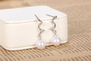 Detail of silver spiral drop earrings with white pearls on a leather jewelry box