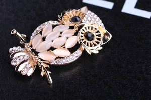 Close-up of golden owl brooch with opal stones and sparkling rhinestones on black background